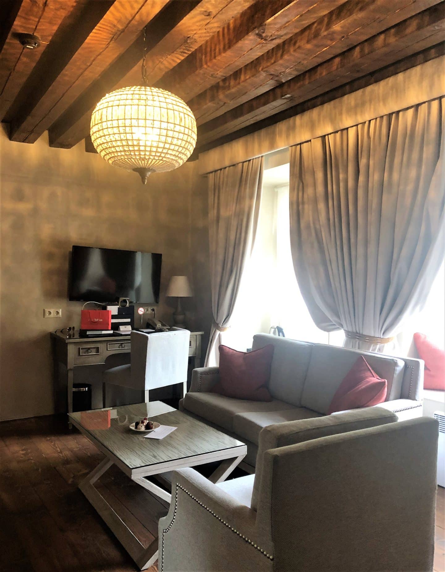 The Schlossle Hotel Tallinn: A view of the grey sofa, armchair, coffee table, desk and TV in the Deluxe Garden Suite 