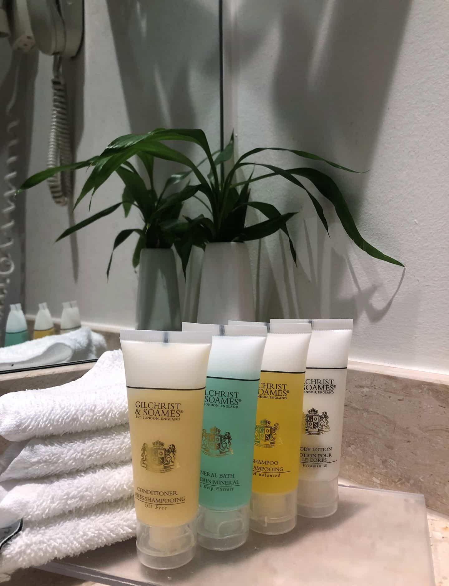 The Schlossle Hotel Tallinn: four plastic containers of Gilchrist & Soames bath products next to fluffy towels in the bathroom in the deluxe garden suite