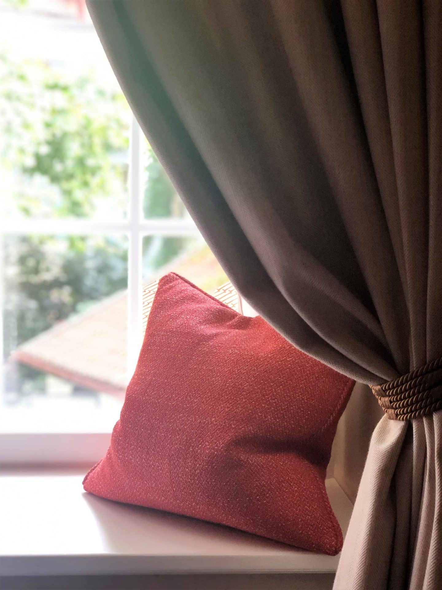 The Schlossle Hotel Tallinn: The stone coloured velvet curtain in the deluxe garden suite with a red velvet cushion laid on the window seat.