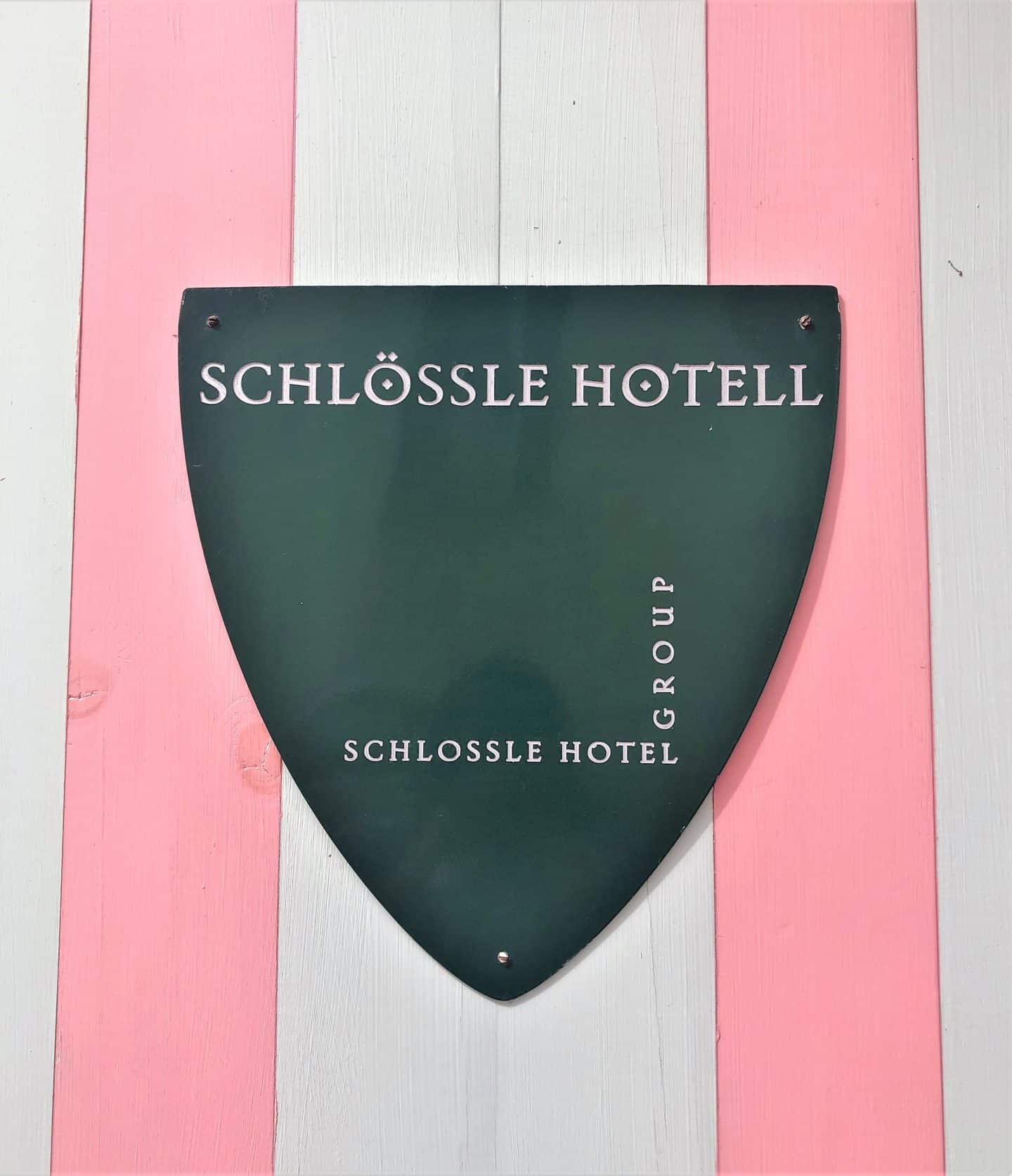 The Schlossle Hotel Tallinn: The black Schlossle Hotel Group shield displayed against the candy pink adn white wodden stripes of a builidng wall.