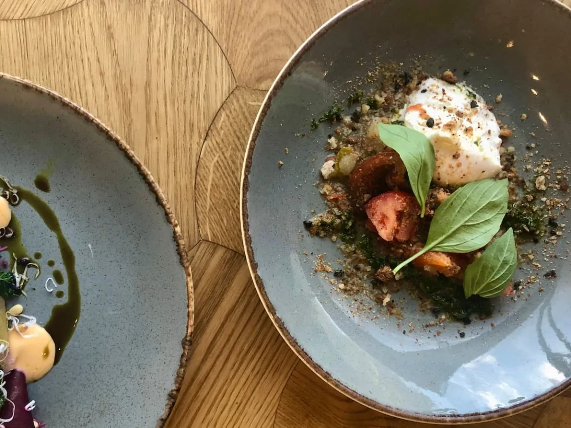 Vegetarian food in Tallinn, Marinated beetroot cuts with vegan cheese, grapefruit mayonnaise, dried kale, pine nuts and pumpkin seed oil. Burrata with fermented tomato and basil pesto. Both dishes are on slate grey earthenware plates.