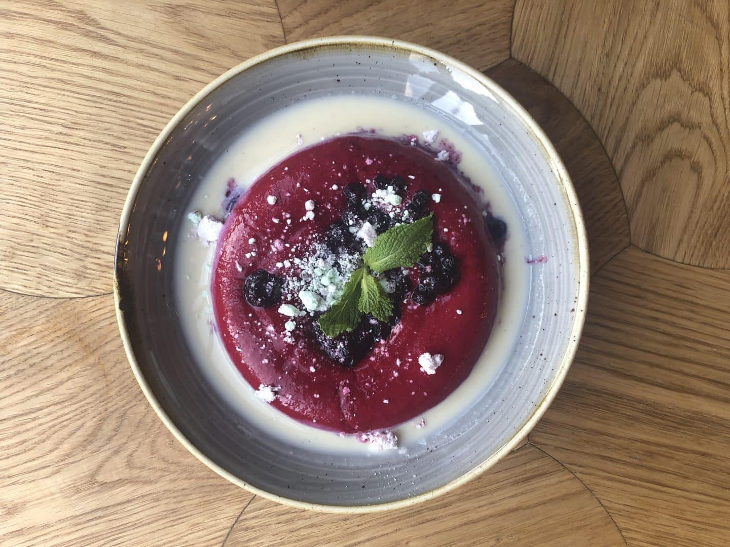 Dessert: Blackcurrant flavoured semolina cream with mint milk, pickled wild blueberries, cardamom and mint meringue. A traditional Latvian dish eaten during the cold war. Served on a light grey plate at Pegasus Restaurant, Tallinn