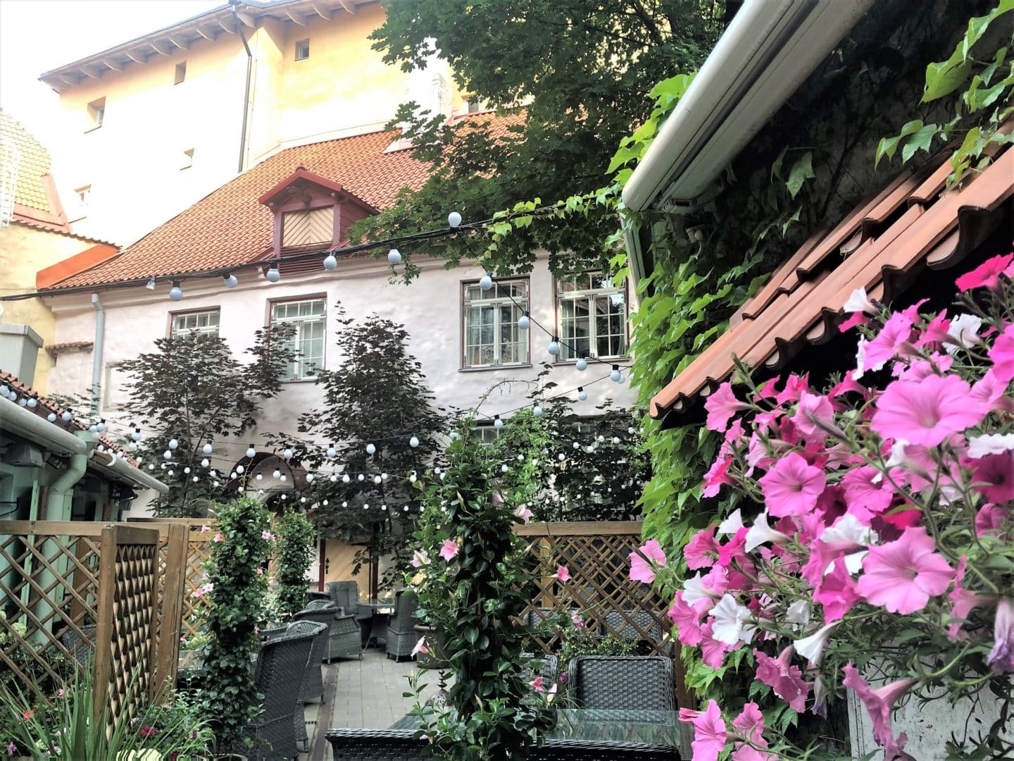 The Schlossle Hotel Tallinn: Alternate view of the summer garden filled with pink flowers and night lights as well as the main hotel building in the background.