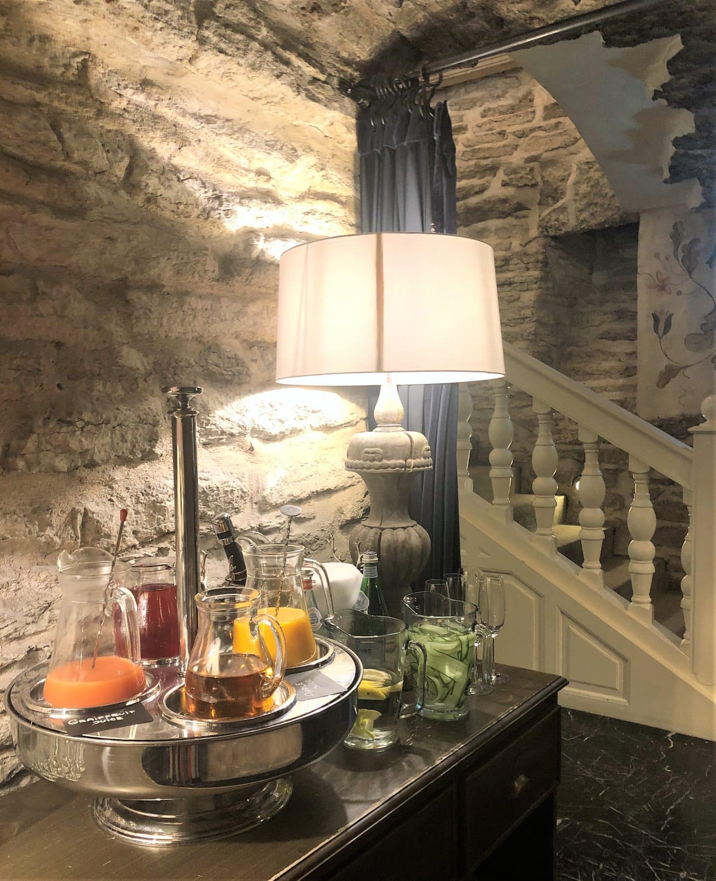 The Schlossle Hotel Tallinn:Jugs of different fresh juices on a dark brown dresser with stairs leading upstairs in the vaulted stoned wall Stenhus restaurant.