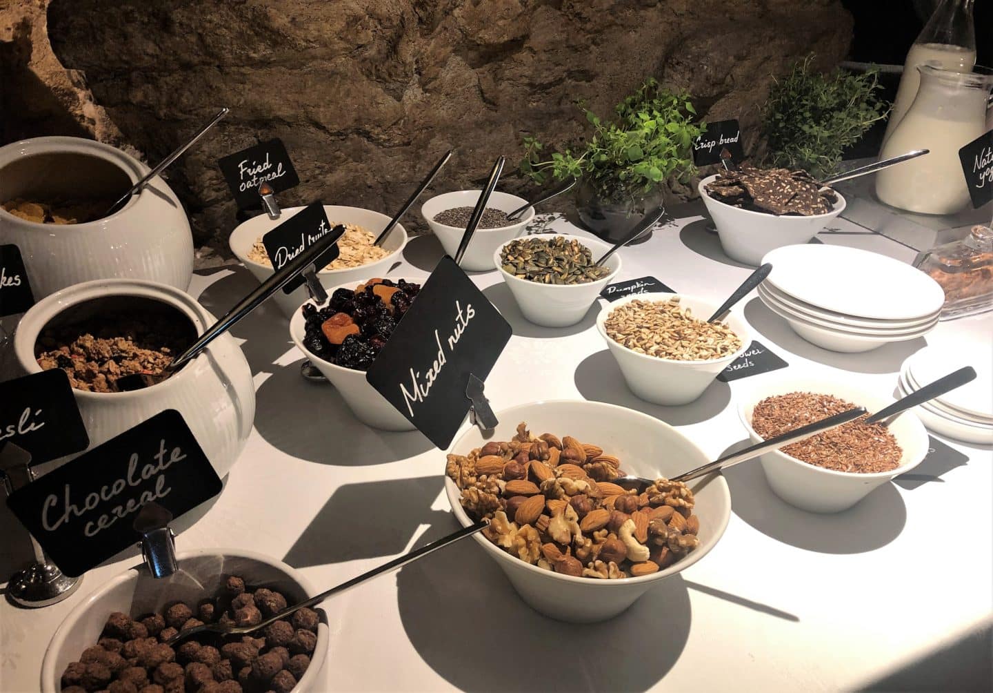 The Schlossle Hotel Tallinn: White bowls containing nuts and cereals against the stoned wall background all laid out on a white table cloth at the Stenhus restaurant.