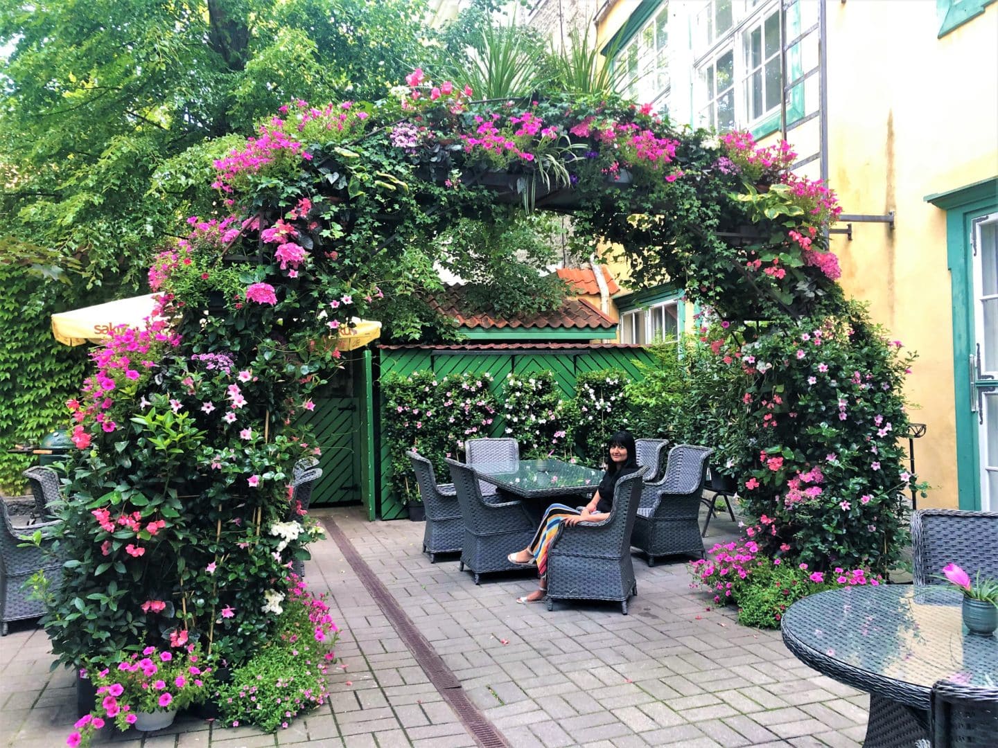 The Schlossle Hotel Tallinn: A green and pink flower archway in the hotel's summer garden with darg grey rattan seating.