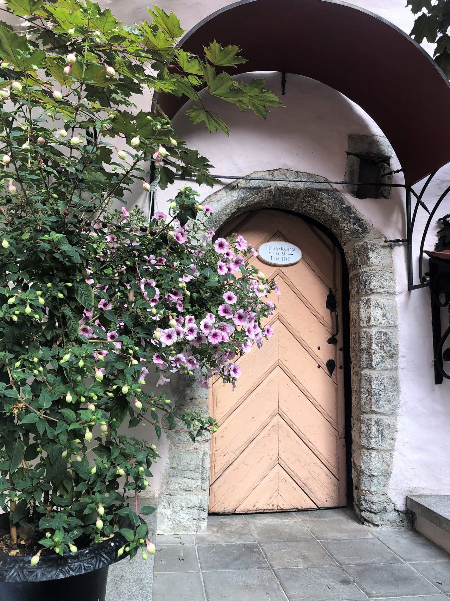 The Schlossle Hotel Tallinn: The medieval beige door that leads into the Sauna with flowers down one side at the entrance of the outer stone wall.
