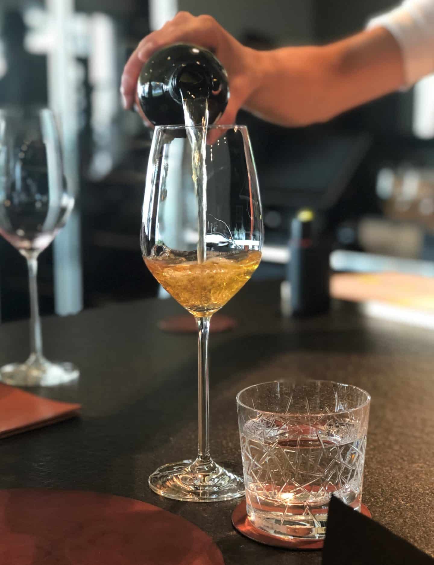 A wine being poured for the amuse bouche course, which is orange in colour at Noa Chef's Hall, Tallinn