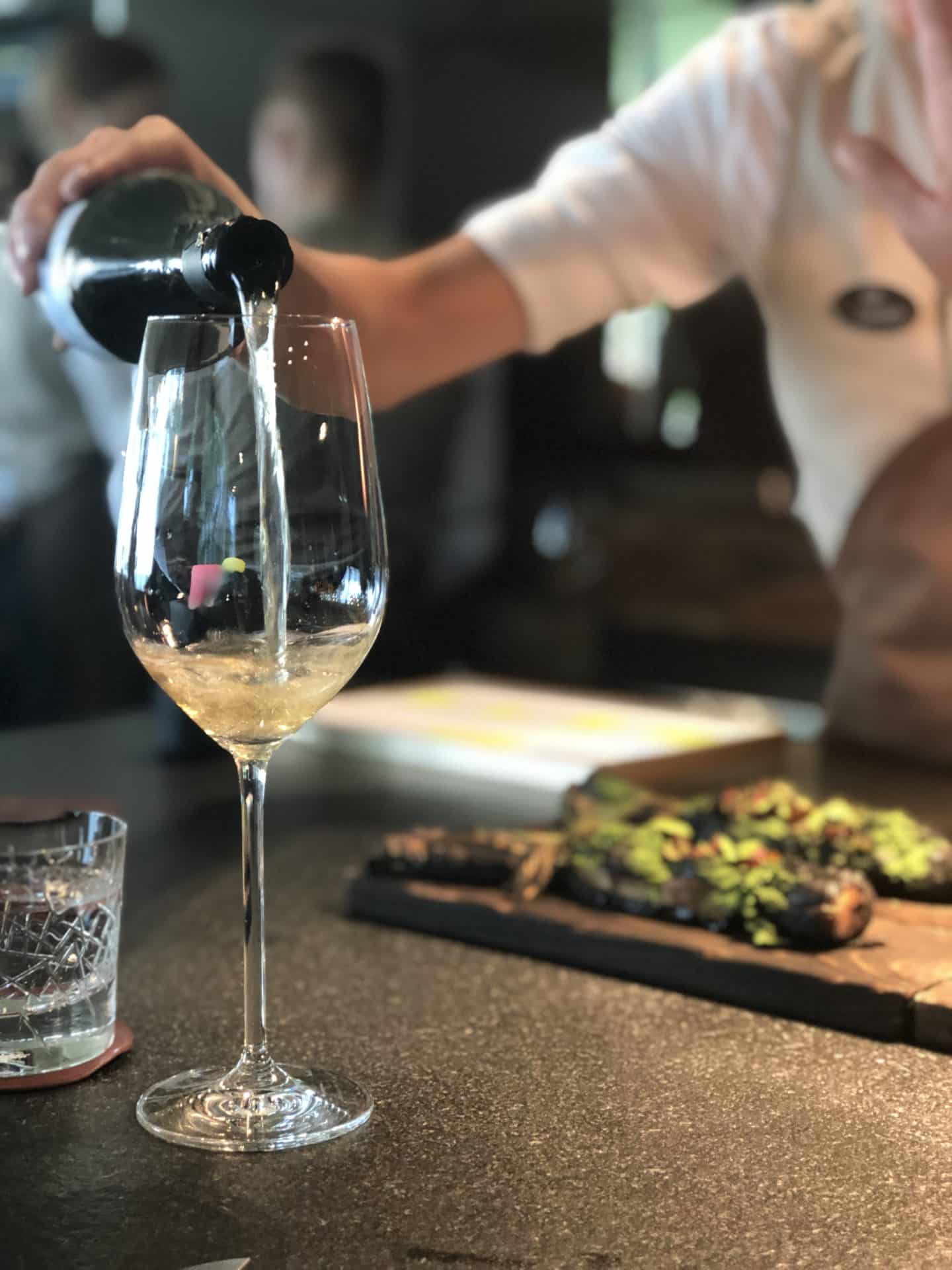 Wine being poured by Sander with boards of charred leeks in the background at Noa Chef's Hall, Tallinn