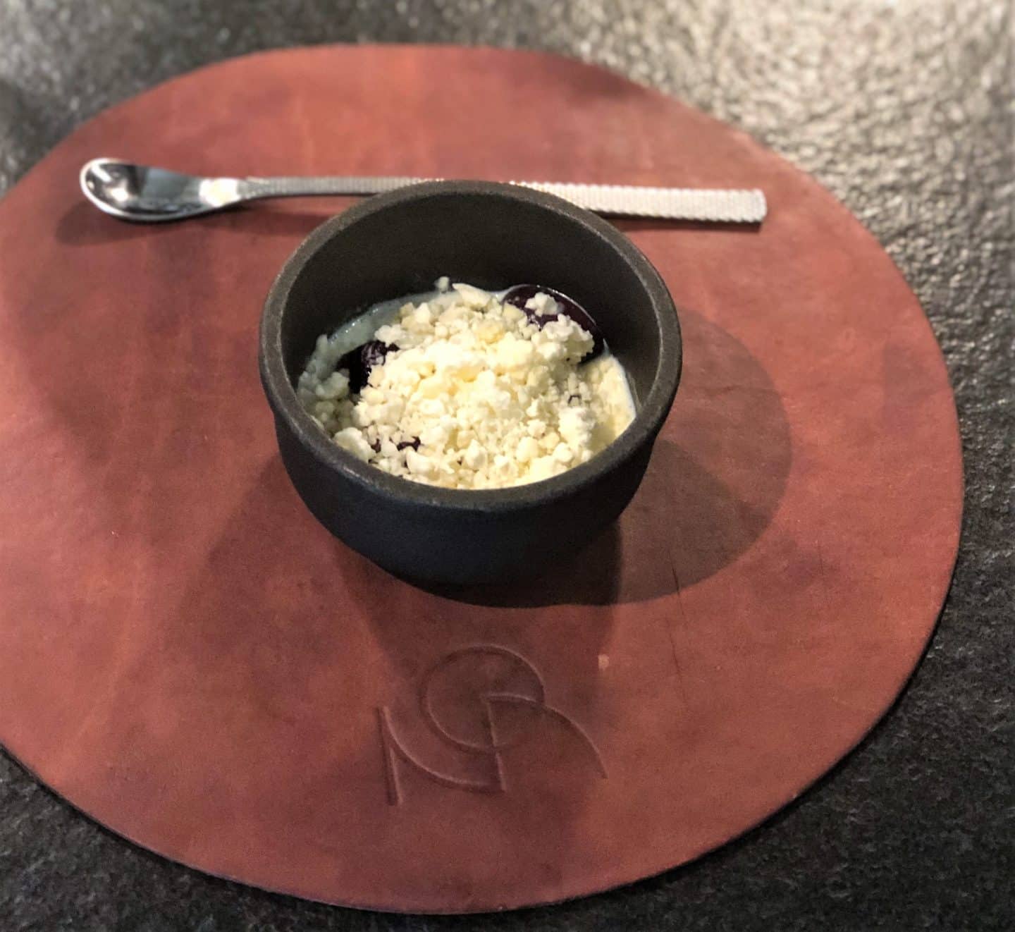 Wild cherries with iced beeswax and plumseed in a small black ramekin at Noa Chef's Hall Tallinn