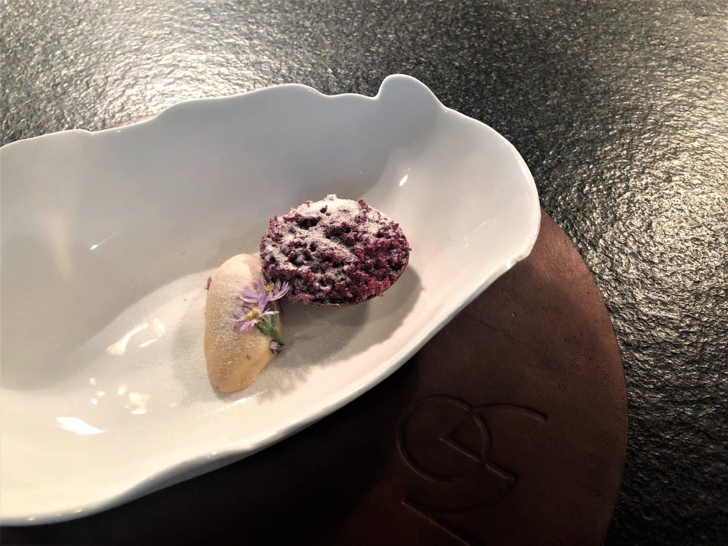 Vegetarian food in Tallinn. Dining at Noa Chefs Hall, Tallinn. Rhubarb and brown butter on a white plate agains a black table surface