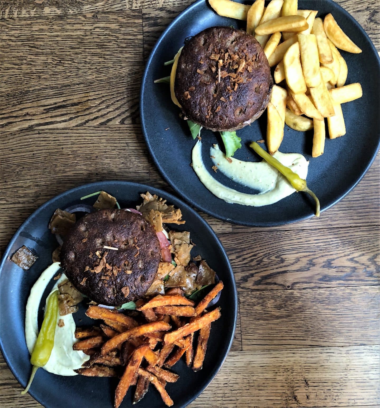Flat lay of vegan Furberger which is a dark bread burger with beetroot hummus, parsley and chilli pepper aioli tomato and red onions and a side of fries on a dark wood table at F-Hoone, Tallinn