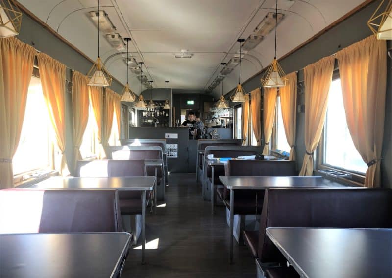 Peatus restaurant carriage in Tallinn. Tables and booths on either side of the carriage with yellow curtains dressing the windows and a serving counter at the end.