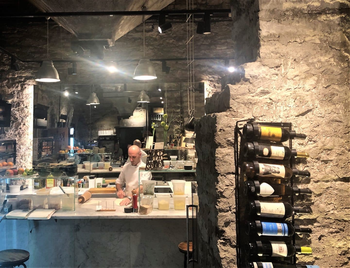 The open kitchen at Flamm with a few bottles of wine on a stone wall with a chef in the background cooking