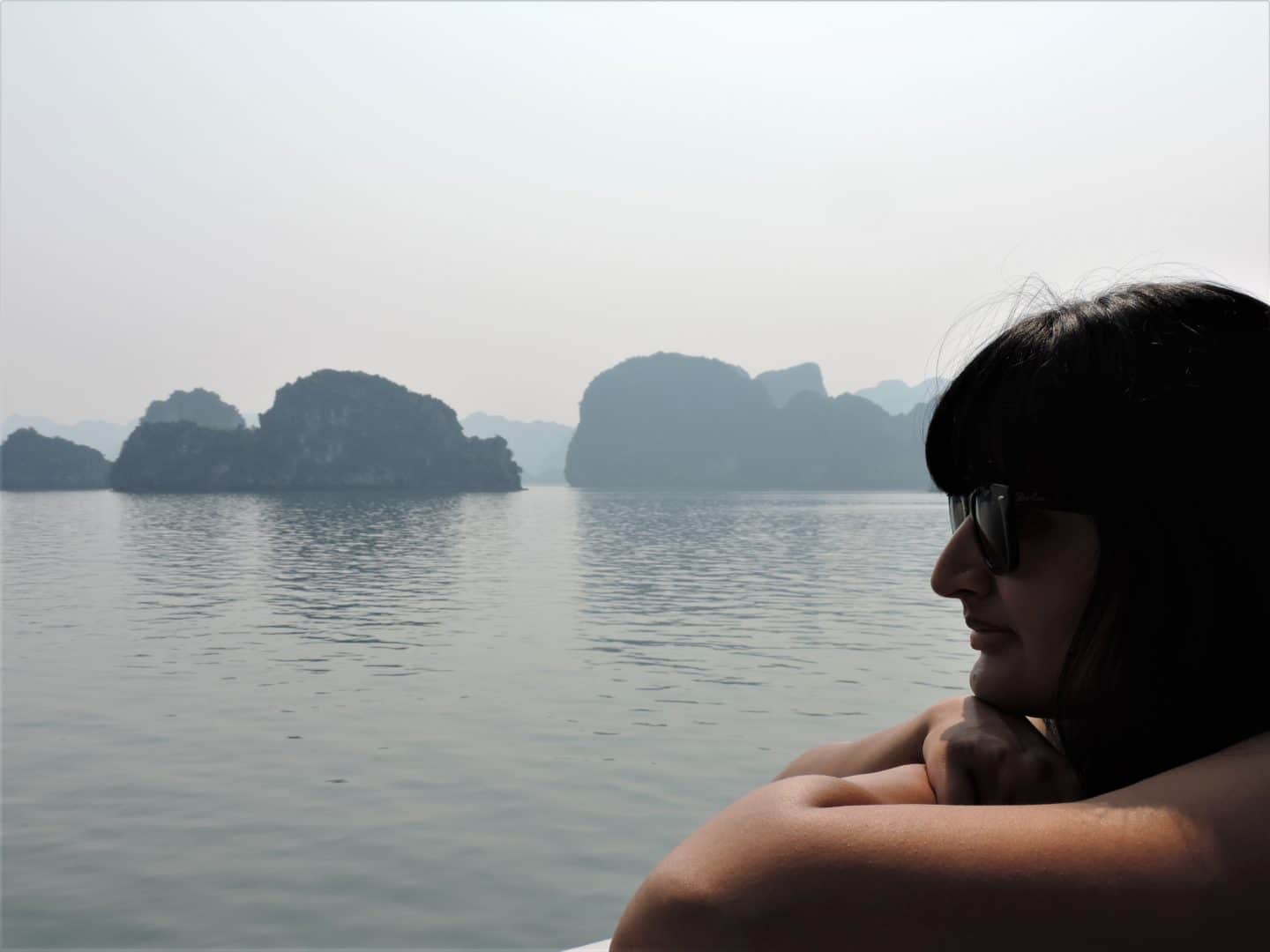 Halong Bay cruise with Bejal sitting on balcony looking out at limestone cliff formations.