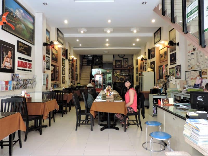 Bejal at Mandarin café in Hue waiting for breakfast with art on the walls for sale and browb table cloths.