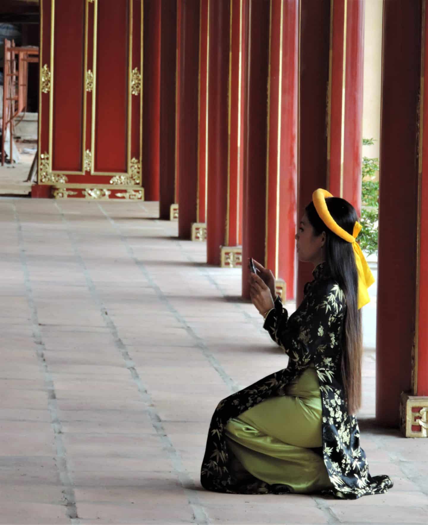 Vietnam in 14 days : Hue Citadel lady in traditional Vietnamese clothing sitting in the surrounding walkways