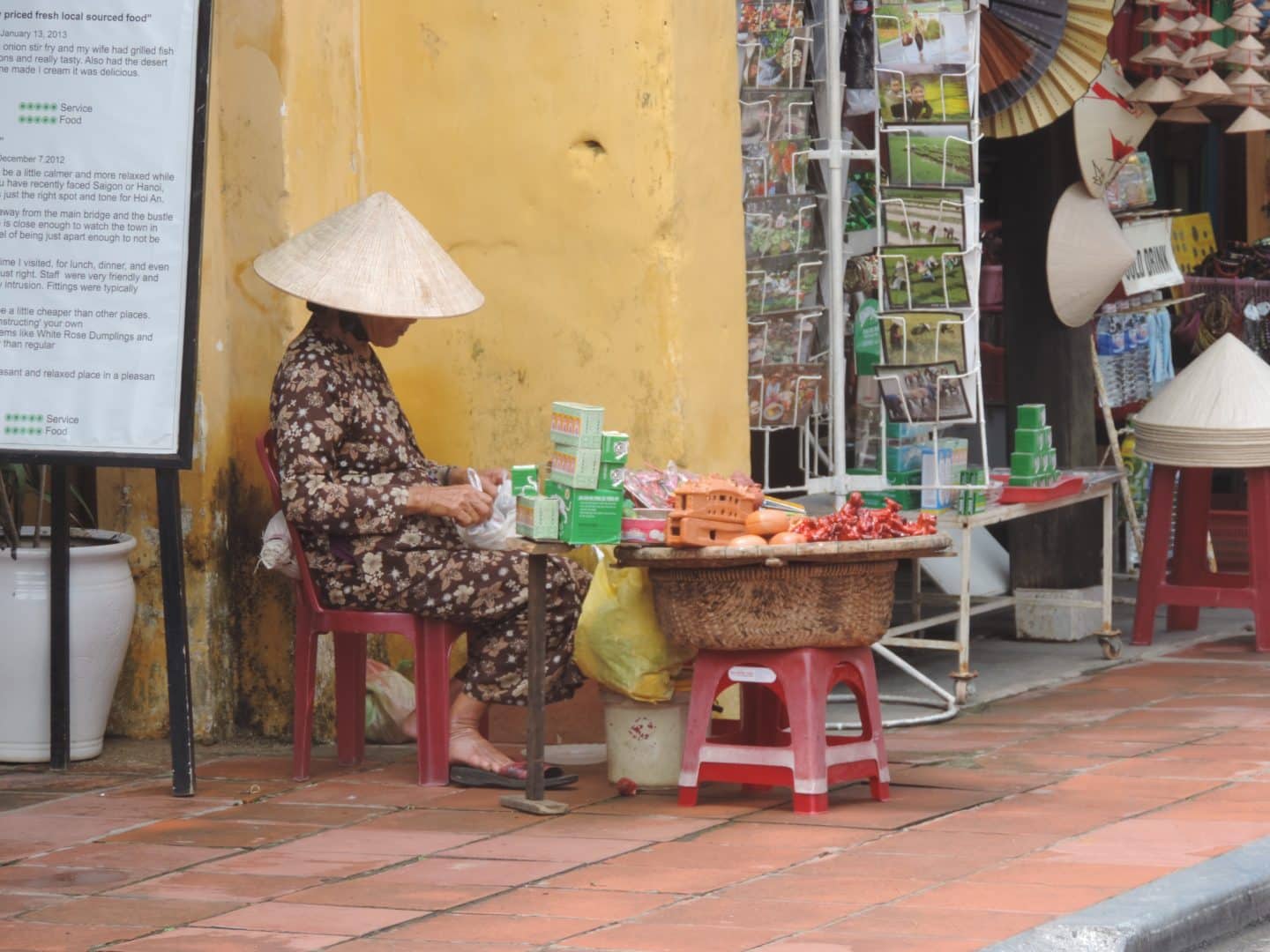 Market trader lady in Hoi An wearing a traditional hat and selling vegetables at the side of the street