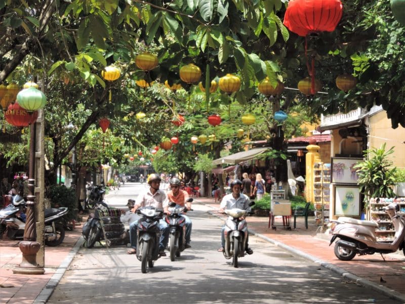 Vietnam in 14 Days: Hoi An motorbikes in road with multi-coloured lanterns above hanging from the trees.