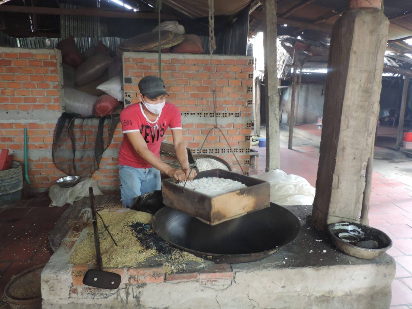 A man wearing a red t-shirt and blue denim jeans making rice pops on the Mekong Delta in Vietnam
