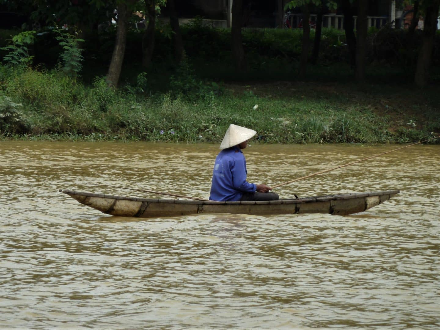 Fisherman on the Perfume River, Hue, in a small boat wearing a traditional bamboo hat and a blue top.