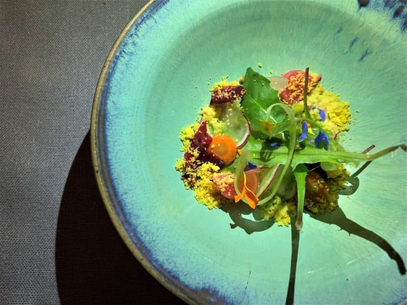 Michelin Starred Dining at Bottega del Buon Caffe, Florence. A turquise dish with colourful edible flowers adn vegetables. The plate is on a grey slate table.