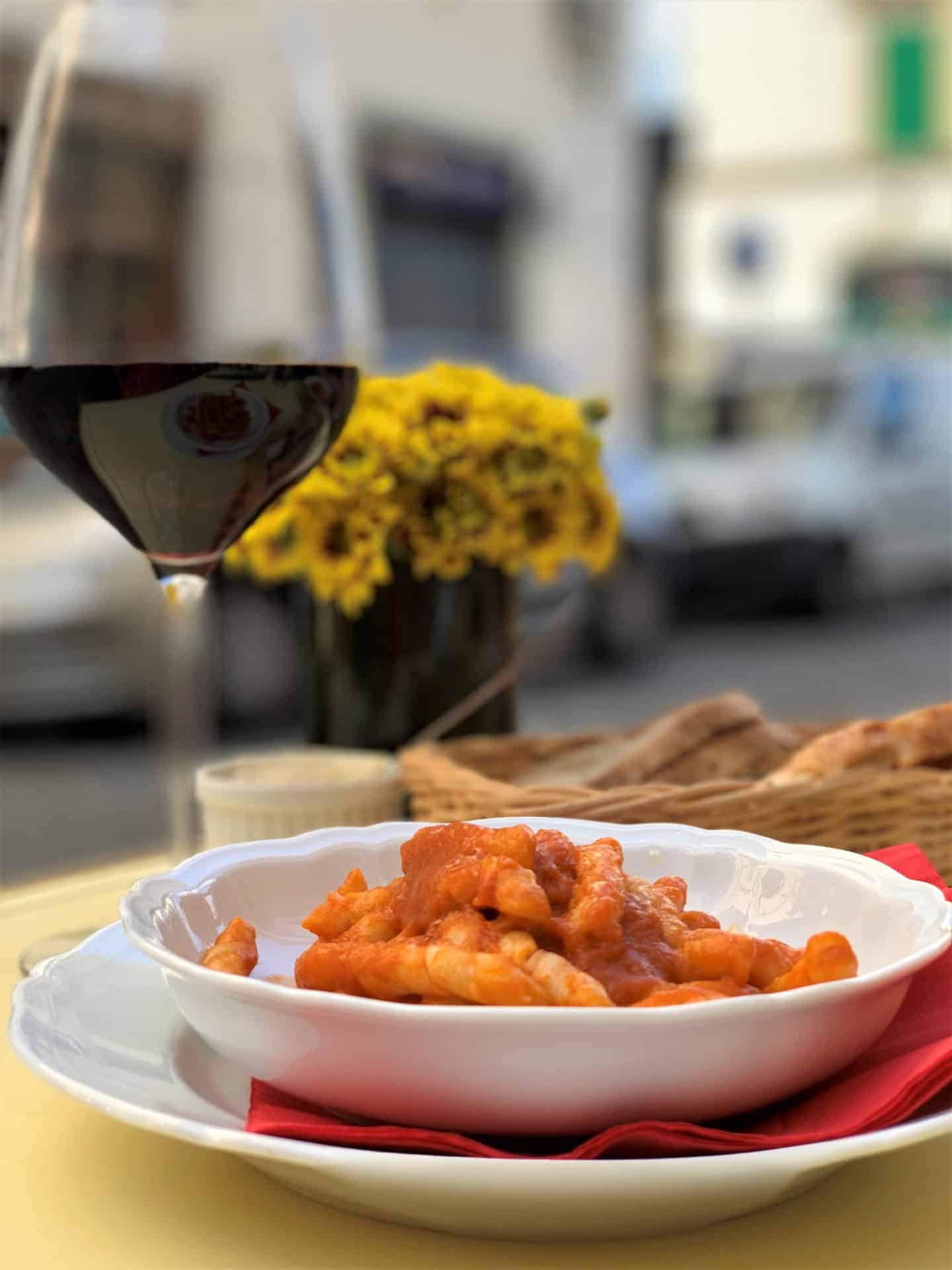 Cibrèo Caffè - pasta with tomato sauce adn a glass of red wine. A vase of yellow flowers. Vegetarian-friendly food in Florence.