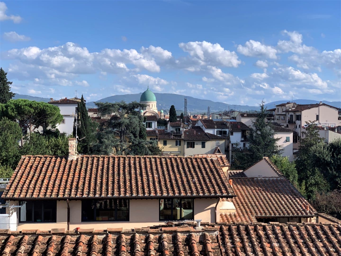 The views of rooftops out of the windows of Caffè del Verone. Loggias and a green domed building in the distance with a mountain behind it