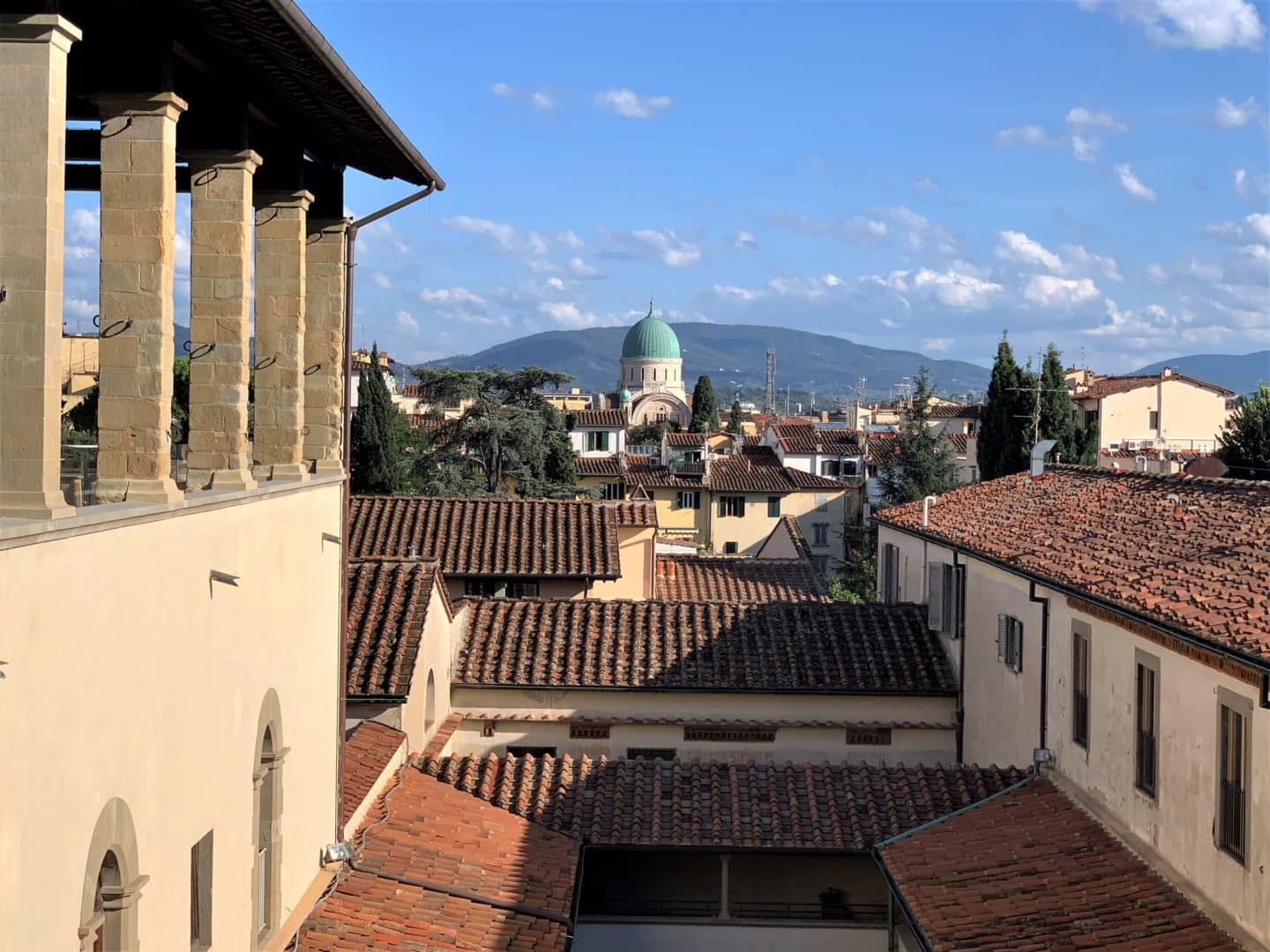 The views of rooftops out of the windows of Caffè del Verone. Loggias and a green domed building in the distance with a mountain behind it