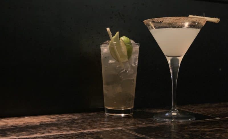 A Mezcal Gingerita and Chilicano Cocktail on a wooden counter with a black background.