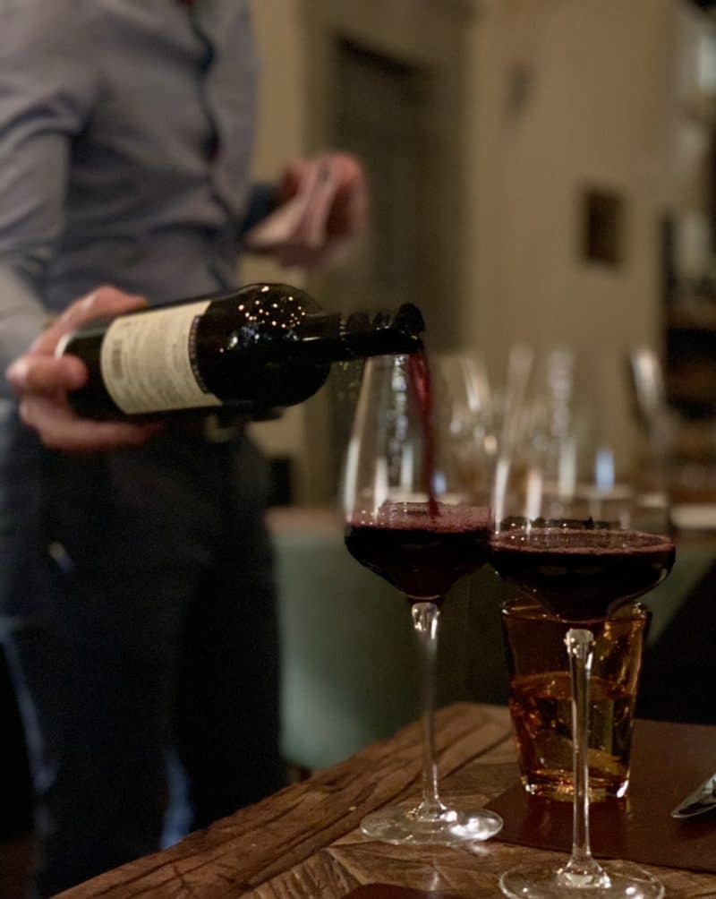 Vegetarian-friendly food in Florence. Waiter pouring red wine into wine glass at Konnubio restaurant