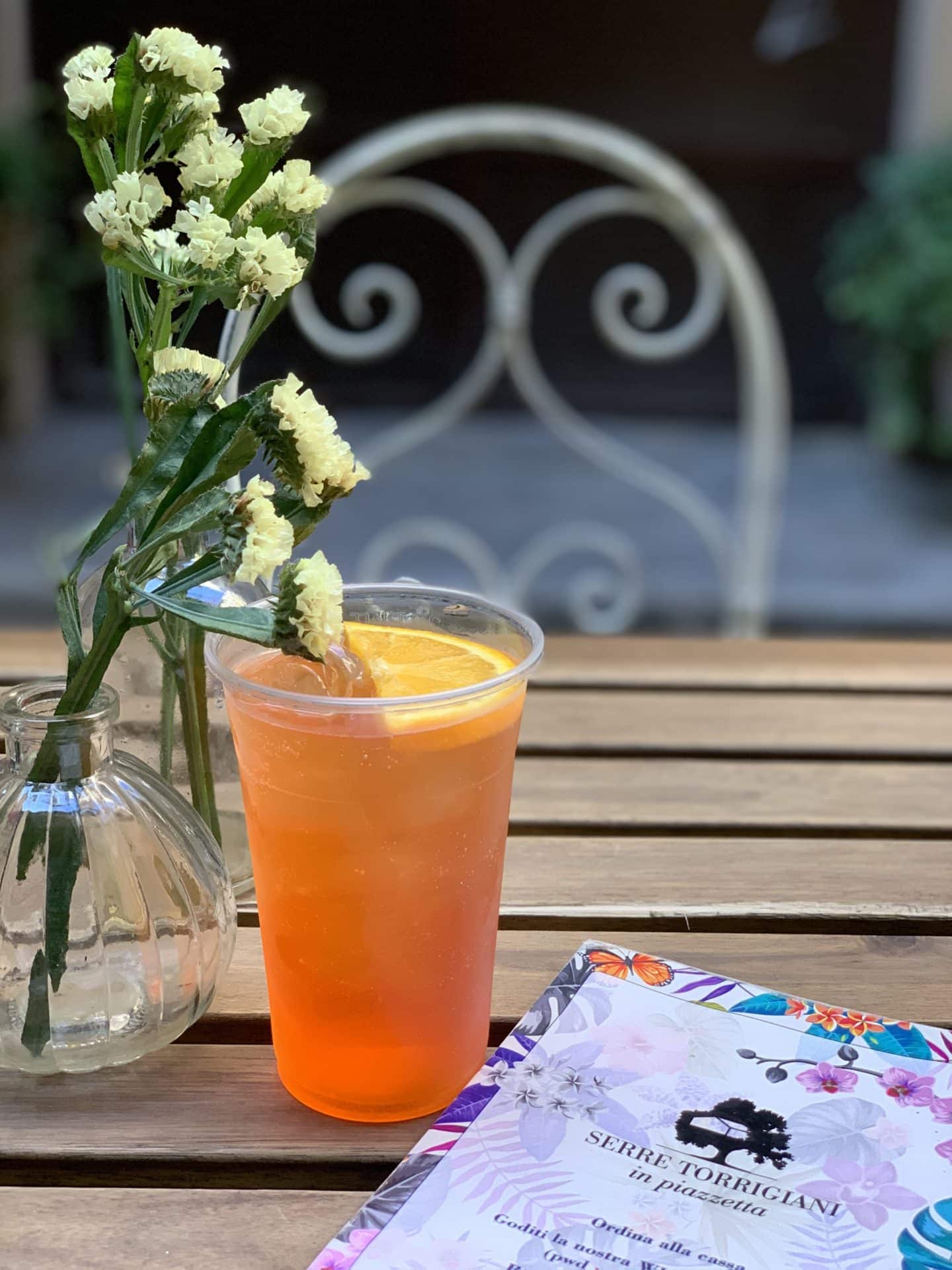 Serre Torrigiani in Piazzetta - Glass of Aperol Spritz with. avase of yellow flowers.