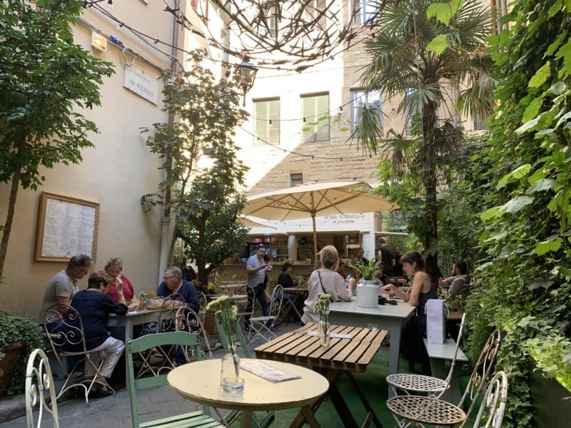 Serre Torrigiani in Piazzetta - The garden area courtyard of the outdoor bar with tables and people sitting drinking in Florence.