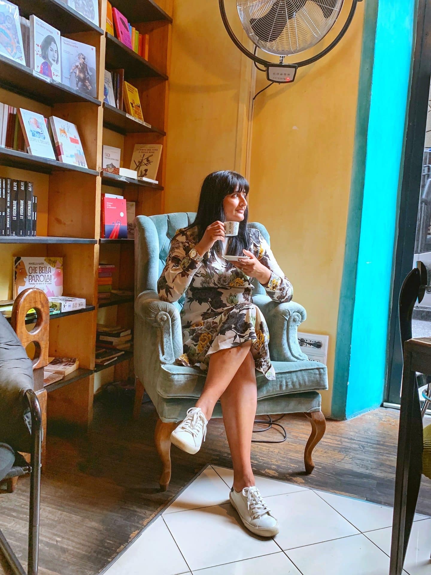 Bejal sitting on an armchair surrounded by books adn mustard yellow walls at Libreria Cafè La Cité