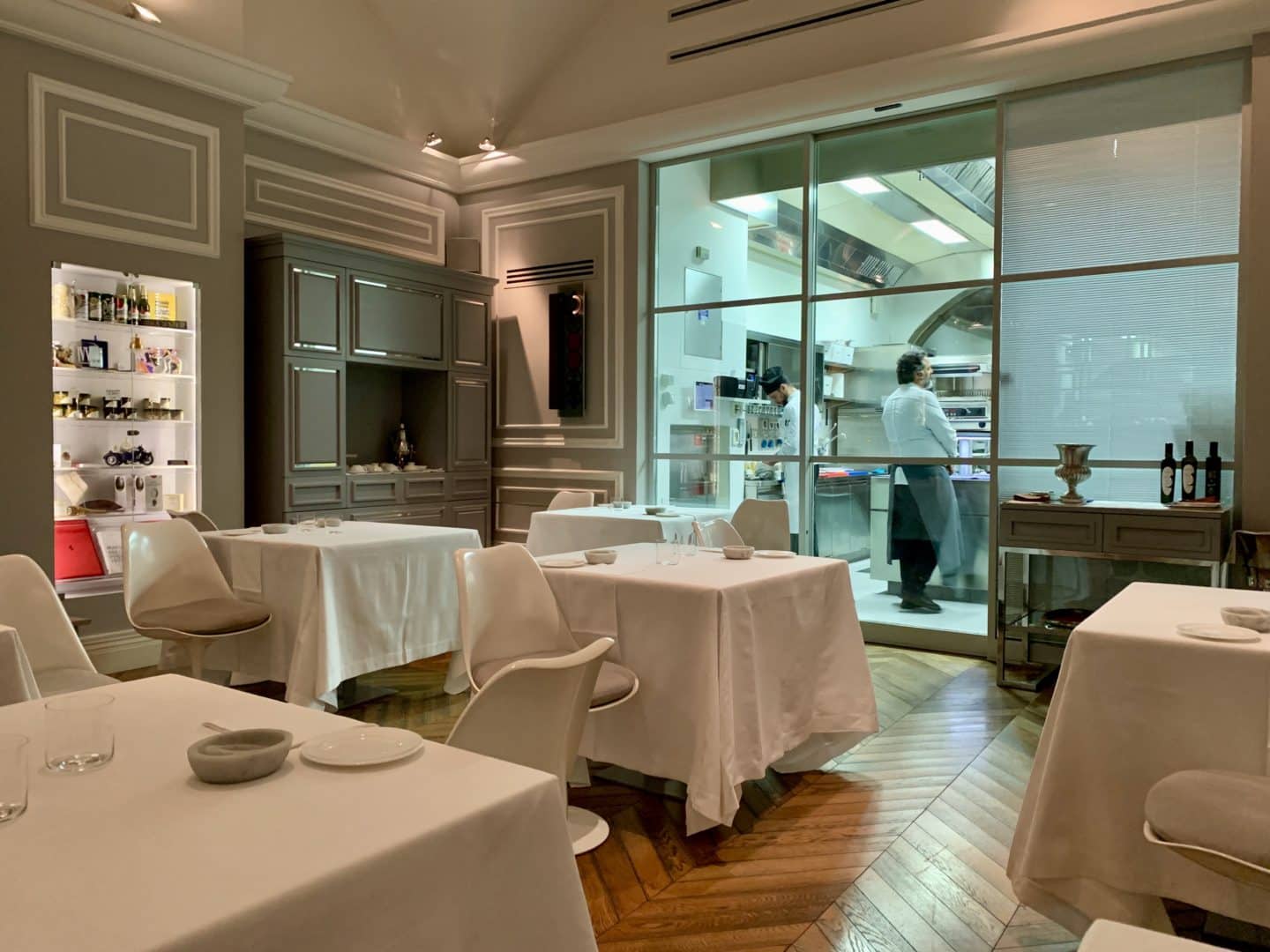 The interiors of Ora D'aria. Modern and contemporary white table clothes with sliding transparent doors through to the kicthen