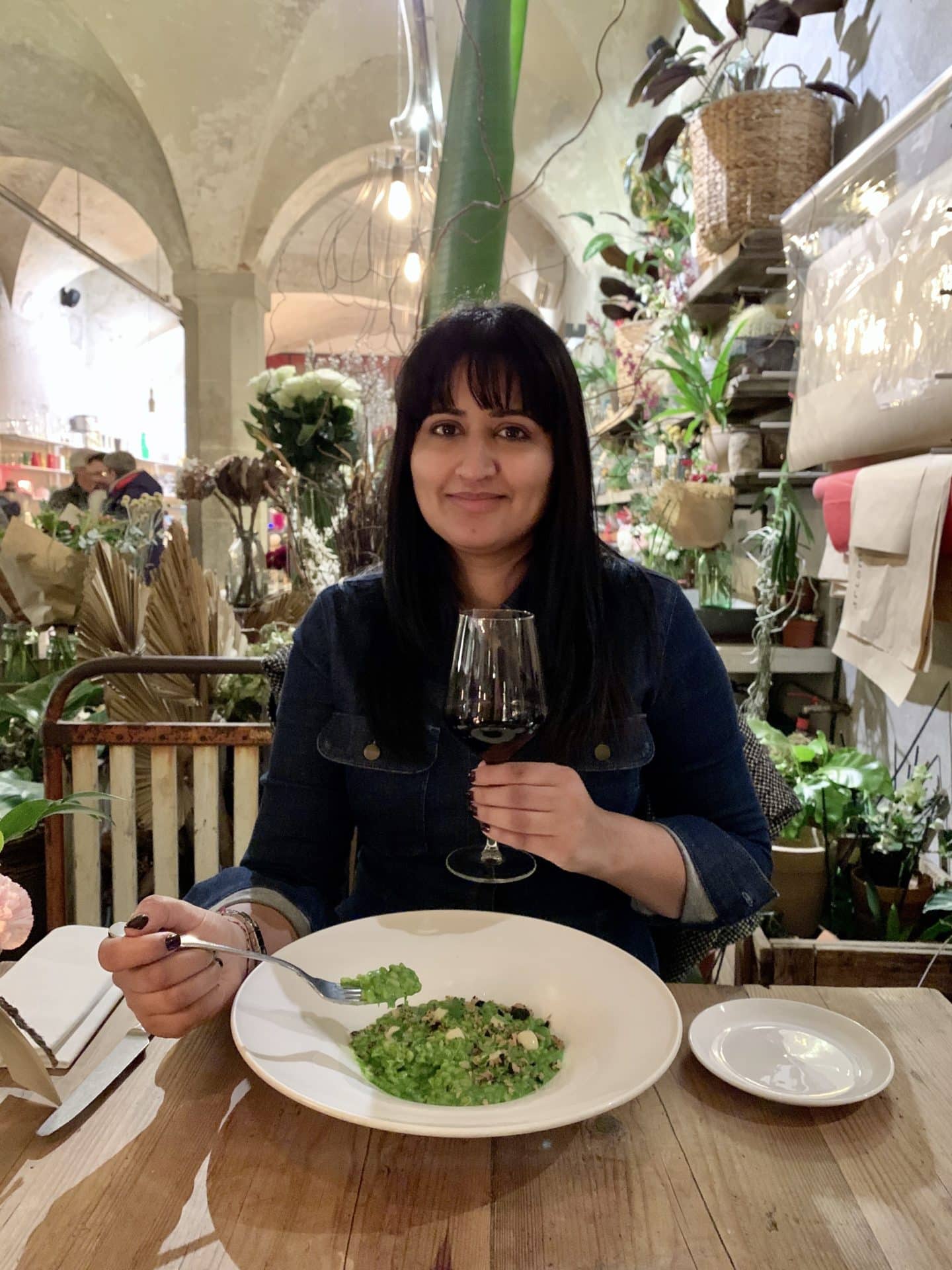 La Ménagère - Bejal sitting eating Gnocchi  with a red wine glass in one hand.