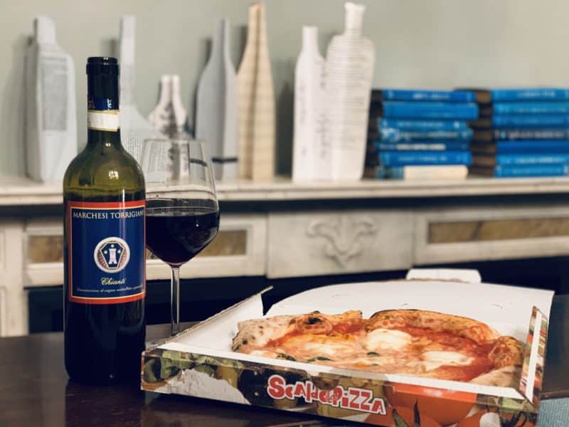 Gusta Pizza with Margherita in box with a bottle of red wine and a red wine glass next to pizza box. At Ad Astra Hotel Room