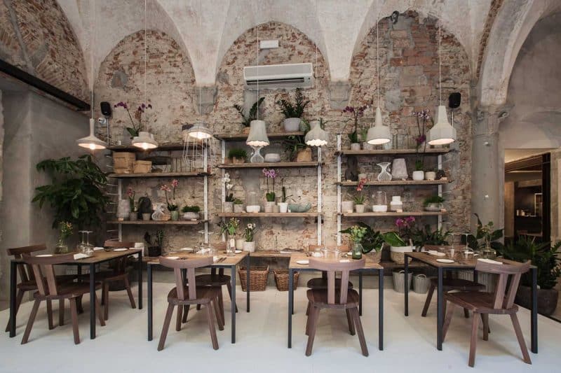 The arched stone interiors of La Ménagère. There are 4 tables of 2 set with cutlery adn in the background is a long shelf with potted plants adn jars.