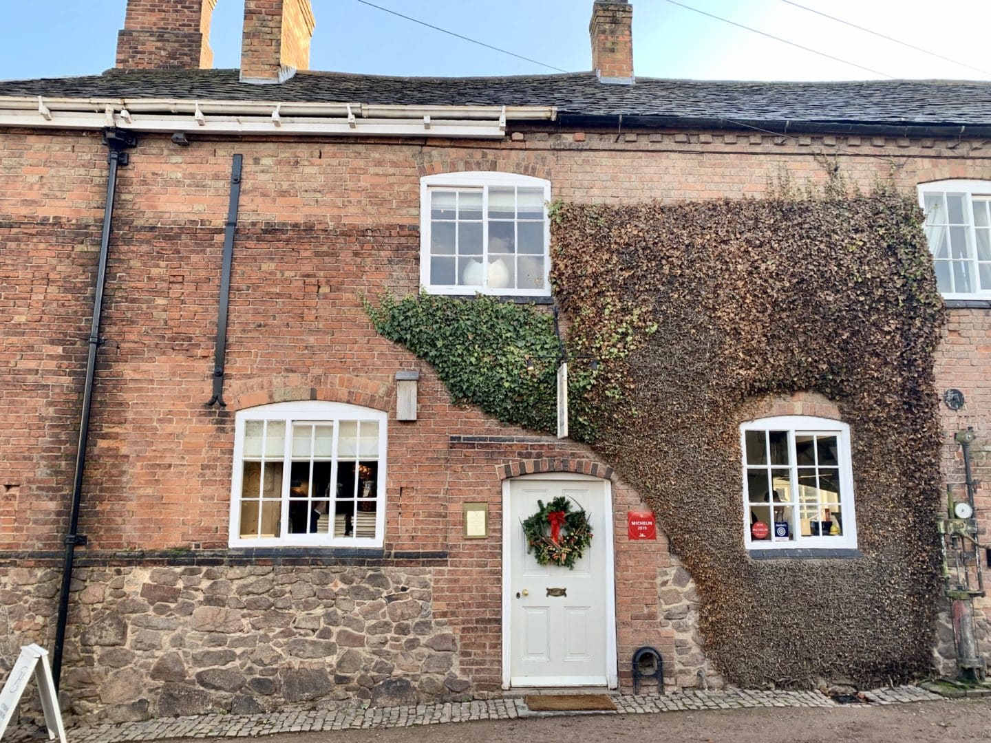 Michelin Star dining at John's House in Leicestershire: The exterios of John's farmhouse made of red brick and half covered in ivy with a white door adn greena and red wreath. 