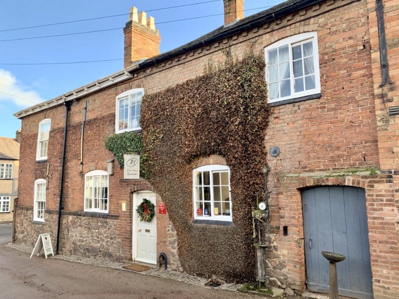 Michelin Star dining at John's House in Leicestershire: the exterior of John's farmhouse in red brick, covered with an ivy wall. There's a grey side door and white front door. 