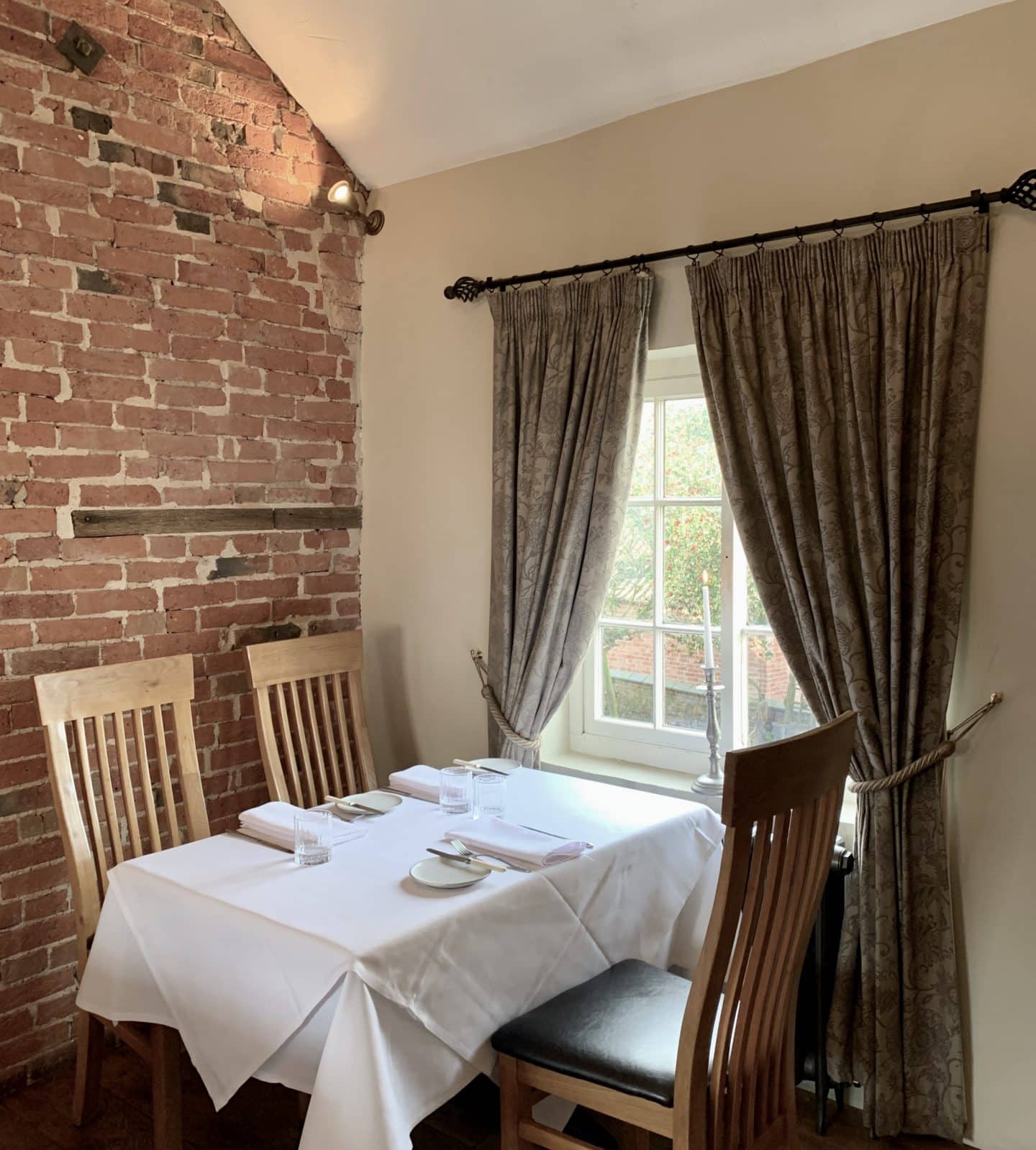 Restaurant area upstairs at John's House with ta table next to the window with floral curtains and a table of 3 set up with cutlery