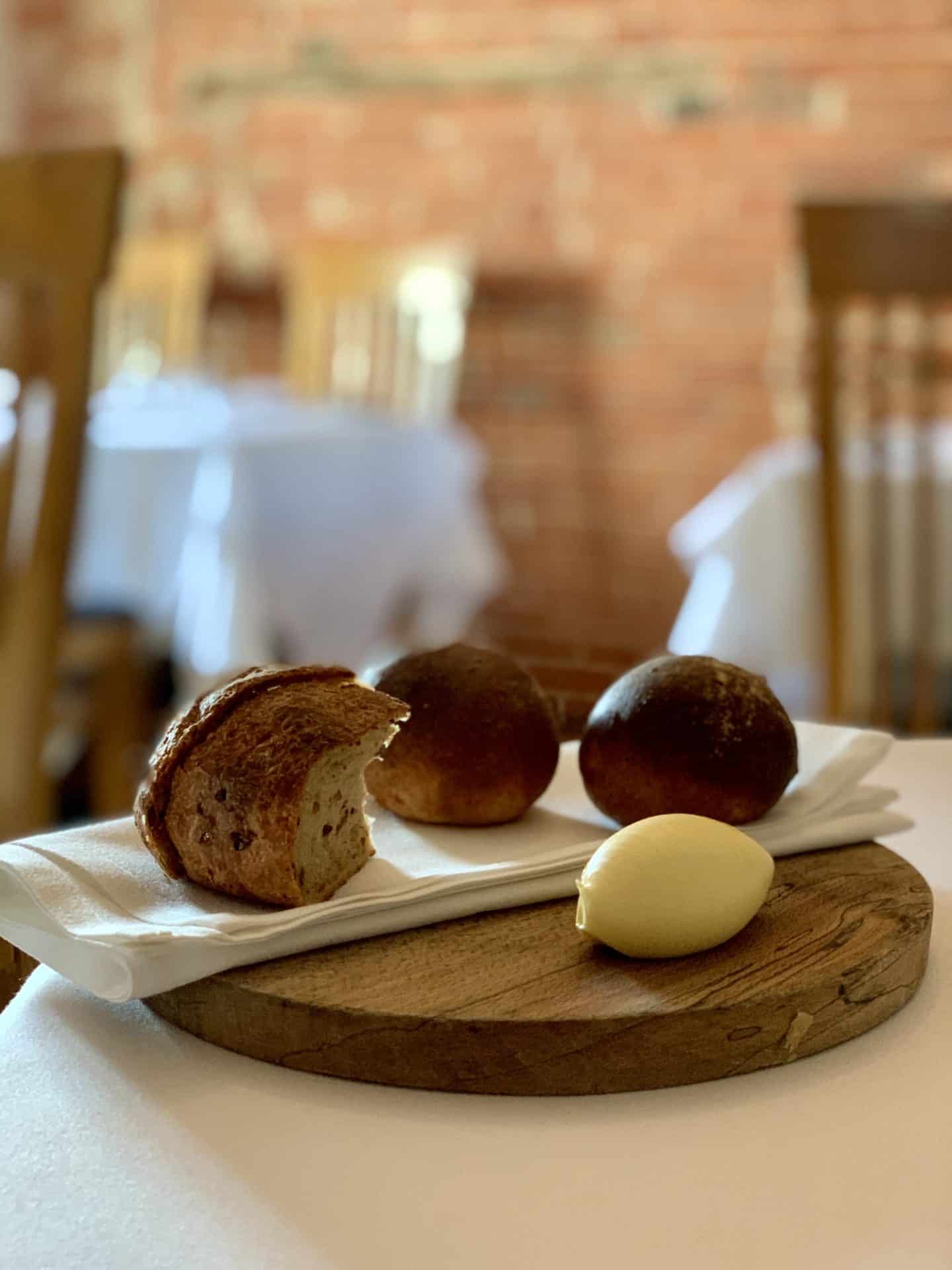 A quenelle of butter on a wooden board with 3 small bread rolls.