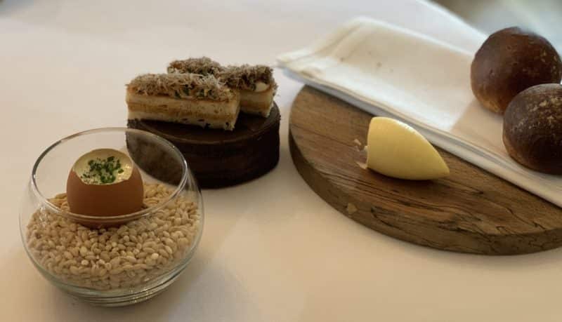 Michelin star dining at John's House in Leicester: truffle custard in  an eggshell in a glass filled with barley and toasties on the side, Butter and bread rolls on the side on a wooden chopping board