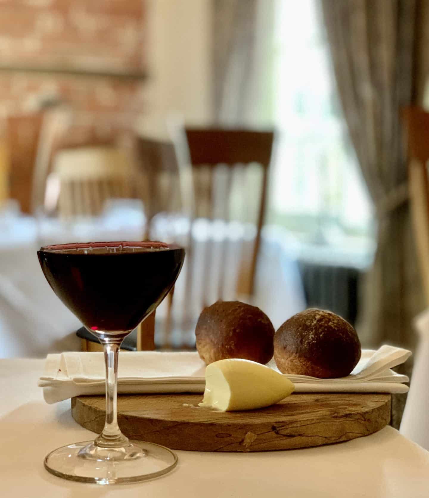 A glass of red wine with bread rolls and butter on a wooden board