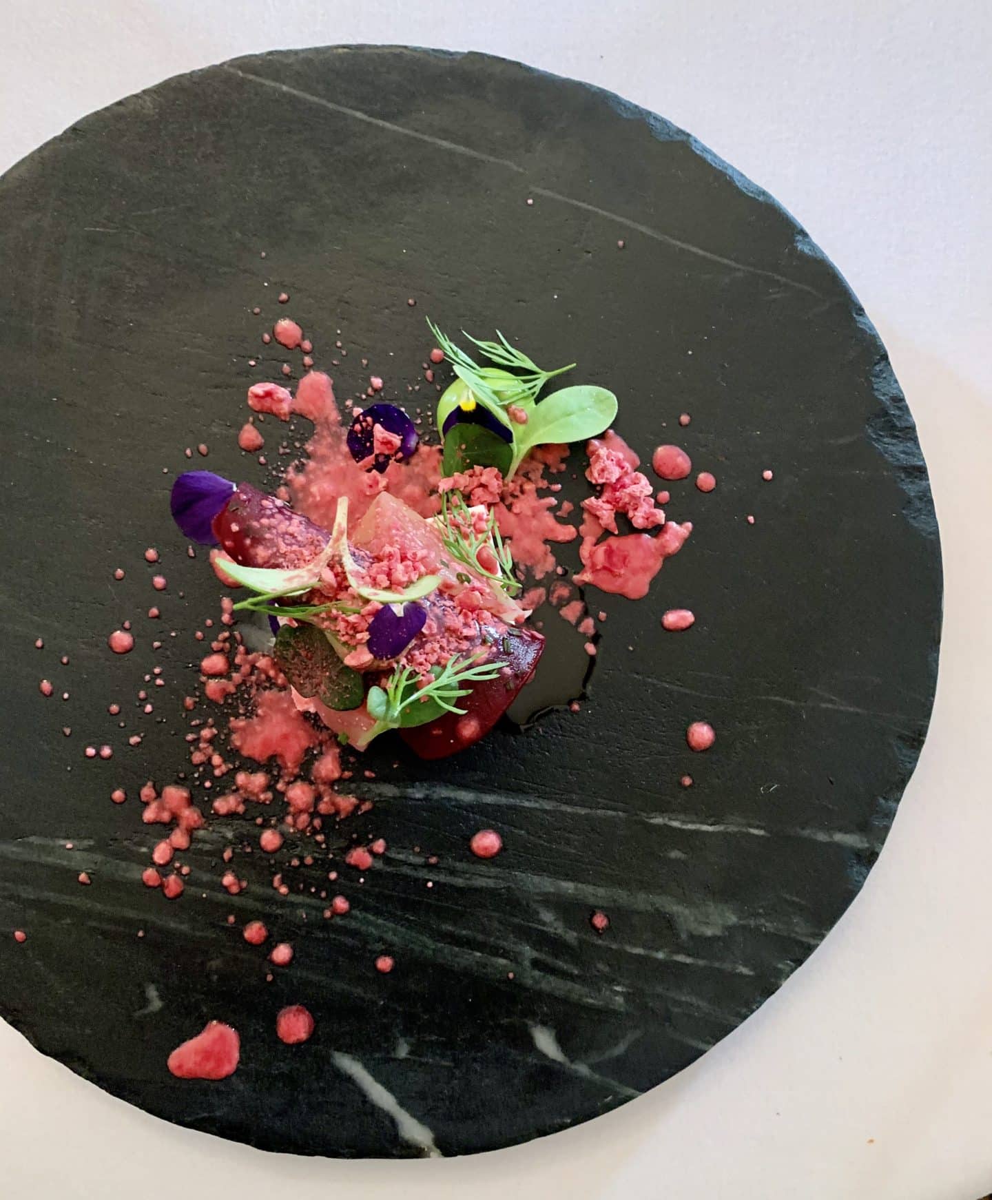 Heritage beetroot on a black slate plate. Bright colours if the deep pink beetroot with green salad leaves