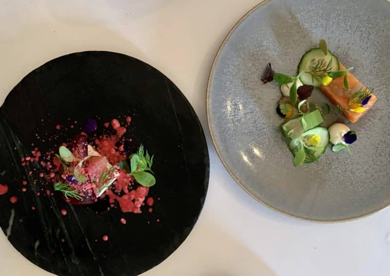 Heritage beetroot on a black slate plate. Bright colours if the deep pink beetroot with green salad leaves and Pastle colours of teh Loch Duart salmon on a light gray plate