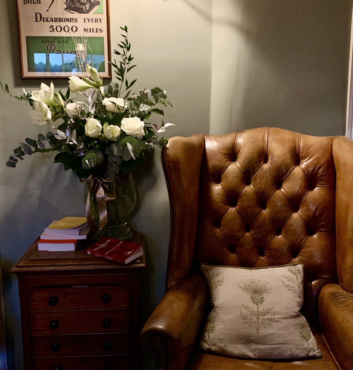 Michelin Star dining at John's House in Leicestershire: A tan chesterfield chair in the lounge area with a vase of white roses on a side table.