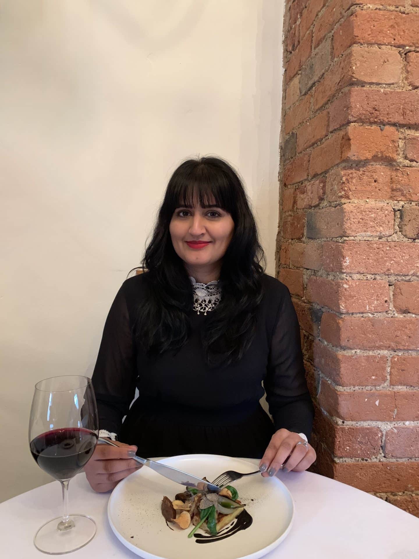 Bejal wearing a black and white dress eating the Truffle Pudding, Hen of the Woods, Artichoke and Chilli 