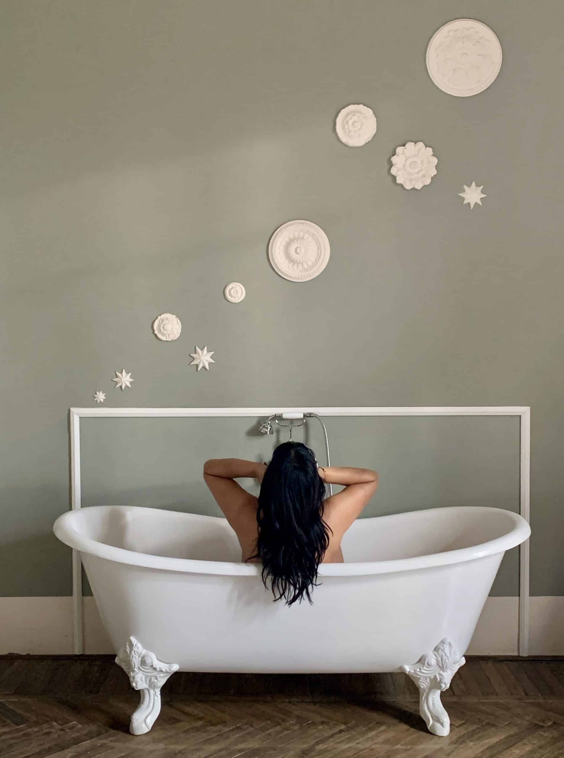 Bejal sat in roll-top bath with white plate son wall