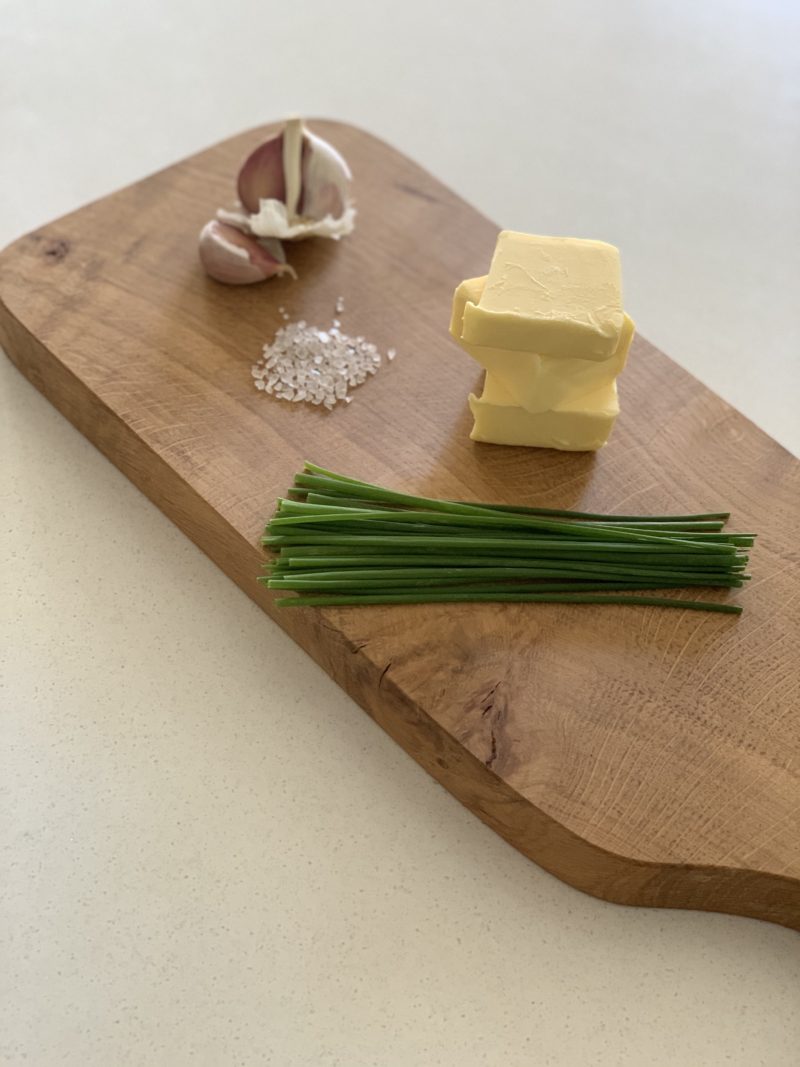 Garlic, chive and herb butter cut into slices on a chopping board with sea salt